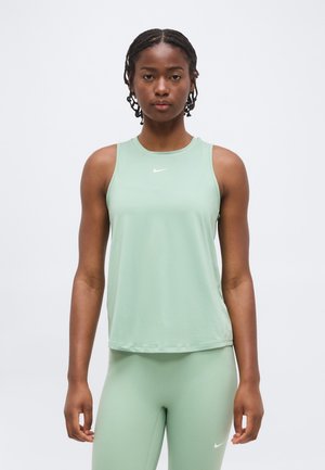 Femme debout portant un haut Nike sans manches vert clair et un legging assorti sur fond blanc uni