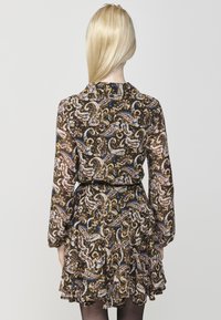 Zwarte lange mouwen jurk met een paisleypatroon in roze, blauw en goud. Heeft een gerimpelde zoom en een getailleerde taille. Zachte, transparante stof.