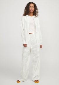 Conjunto de camiseta de rayas blancas y pantalones de pierna ancha, que presenta una textura suave y un ajuste relajado. Combinado con sandalias amarillas, que muestran tonos claros.