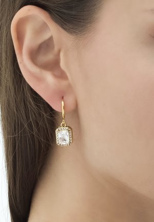 Goldene Creolen mit einem rechteckigen klaren Stein, umgeben von kleinen funkelnden Akzenten, die elegant vom Ohr hängen.