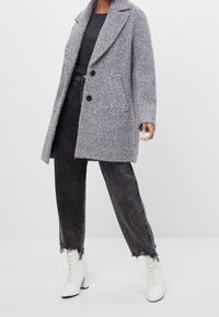 Abrigo de mezcla de lana gris con solapa muesca, dos botones negros y bolsillos laterales. Combinado con vaqueros negros de cintura alta y botas blancas con cordones.