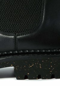 Botte en cuir noir présentant un panneau en mesh texturé, une semelle en caoutchouc contrastante avec un design en liège moucheté, et un détail de couture visible.