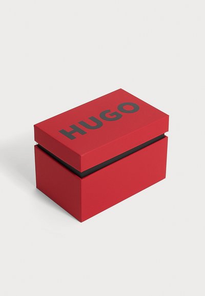 Boîte rectangulaire rouge avec texte noir "HUGO" sur le couvercle, sur un fond clair uni.