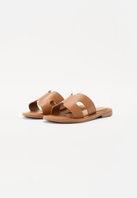 Braune Ledersandalen mit zwei breiten Riemen, die mit Ausschnitten versehen sind, flache Holzsohle und glatter Textur. Langlebiges und offenes Design.