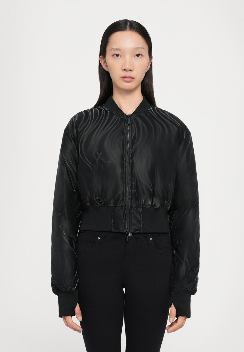Giacca bomber nera con un motivo lucido e vorticoso, chiusura con zip, polsini e orlo a coste, design cropped, abbinata a jeans neri.