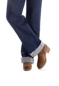 Stivaletti in suede marrone con tacco a blocco corto, abbinati a jeans di denim scuro arrotolati con un risvolto azzurro chiaro.