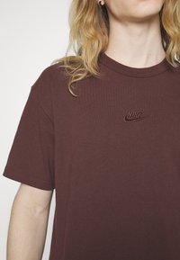 Bordová tričko Nike s krátkými rukávy a kulatým výstřihem. Na hrudi má vyšívané logo. Hladká textura bavlněné látky.