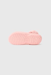 Rosa gummisula på ett barnklädesträd med ett texturerat mönster och en fluffig pom-pom fäst nära hälen.