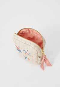 Quiltet beige pose med rosa fôr, blomsterbroderi i rosa og blått, gullglidelås og rosa bånddekorasjon på siden.