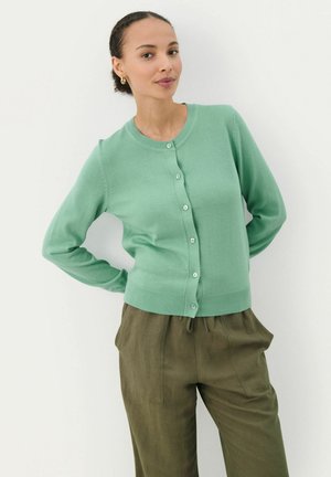 Muntgroene cardigan met een ronde halslijn, knoopsluiting en geribbelde zoom. Gecombineerd met lichtbruine, loszittende broek.
