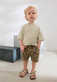Beige póló, barna leopárdmintás sort zsebekkel és bézs szandál, csatokkal. Simább anyag, laza dizájn és kényelmes szabás.