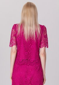 Robe en dentelle fuchsia à manches courtes, présentant des motifs floraux complexes et une silhouette ajustée, mettant en valeur un design texturé et superposé.