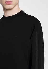 Sweatshirt nero realizzato in tessuto misto cotone, caratterizzato da un collo rotondo, un delicato logo decorativo e strisce laterali testurizzate con dettagli del marchio.