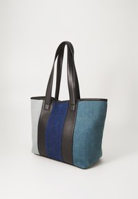 Sac fourre-tout en denim de couleur gris clair, bleu et bleu foncé. Poignées et garnitures en simili cuir noir. Forme rectangulaire avec un haut ouvert.