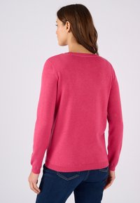 Rosa gebreide trui met lange mouwen, ronde hals en geribbelde manchetten. Glad textuur; gedragen met blauwe denim jeans.