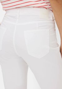 Witte jeans met een gladde textuur, voorzien van twee achterzakken en een label op de tailleband. De pasvorm is aansluitend.