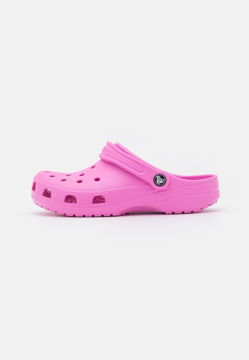 Sabot rose à enfiler avec des trous de ventilation, une semelle texturée et une bride de talon réglable avec un bouton rond à logo sur un fond uni.