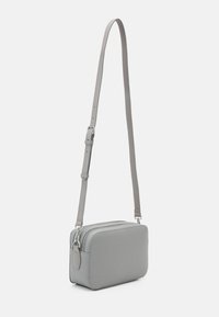 Borsa a tracolla in pelle grigia con tracolla regolabile, forma rettangolare, chiusura con cerniera, superficie testurizzata e un dettaglio decorativo in metallo.