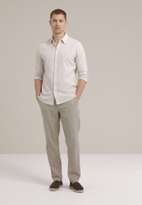 Camisa de lino gris claro con botones y mangas largas, combinada con pantalones ligeros beige y zapatos oscuros de tacón.