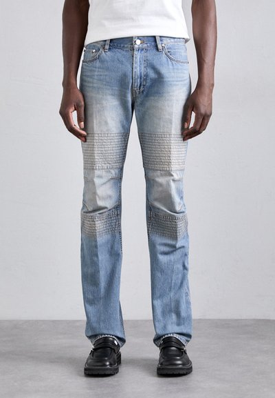 Svetle modré džíny z denimu s tapered střihem, které mají texturované akcenty z patchworku a detaily s obarvením. Dokončeno klasickým pětipocket stylem.