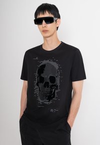 Camiseta de algodón negra con un diseño gráfico de calavera pixelada en tonos de gris, combinada con gafas de sol angulares negras.