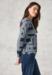 Felpa blu navy con motivi geometrici bianchi, maniche lunghe e colletto a girocollo. Tessuto morbido con una vestibilità rilassata e orlo a coste.