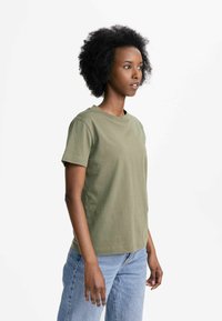 Olivenfarbiges Baumwoll-T-Shirt mit kurzen Ärmeln, Rundhalsausschnitt, lockerer Passform, getragen mit hellblauen Denim-Jeans. Einfaches und grundlegendes Design.