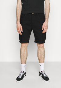 Černé cargo šortky s dvěma bočními kapsami, nastavitelným pasem a rovný střih. Nosené s černými teniskami a bílými ponožkami.