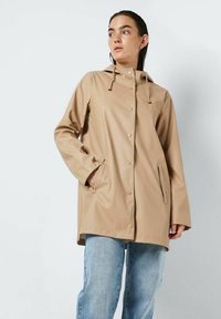 Manteau de pluie beige imperméable avec capuche, fermeture à pression et poches latérales, présentant une texture lisse et un design léger.