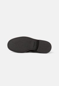 Suola di scarpa nera in gomma testurizzata, forma leggermente curva, con un'impronta del logo e senza hardware o dettagli prominenti.