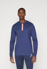 Laivastonsininen pitkähiha Shirt, jossa on vaaleanpunainen korostustunnus kauluksessa ja "NIKE"-logo hihassa. Sileä pinta, rento muotoilu ja istuva malli.