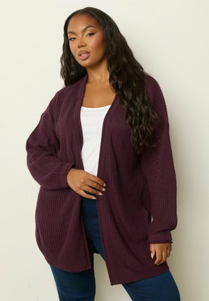 Cárdigan de punto burdeos con frente abierto, mangas largas y textura acanalada. Combinado con una blusa blanca y jeans azules. Ajuste suave y relajado.