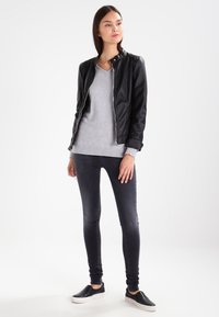Zwarte leren jas met ritssluiting, grijze trui, donkere skinny jeans en zwarte instappers. Glad materiaal, minimalistisch ontwerp.