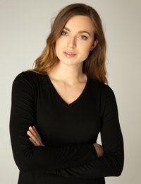 Zwarte lange mouwen top met een V-hals. Stof lijkt glad en zacht. Model heeft de armen gekruist, wat een ontspannen pasvorm toont.