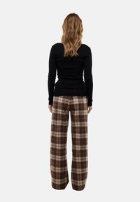 Haut à manches longues noir ajusté associé à un pantalon ample à carreaux brun et beige, présentant une texture douce et des jambes larges.