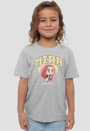 Young girl with curly hair smiles wearing a grey T-shirt with "MIRA" and an anime character inside a heart graphic.