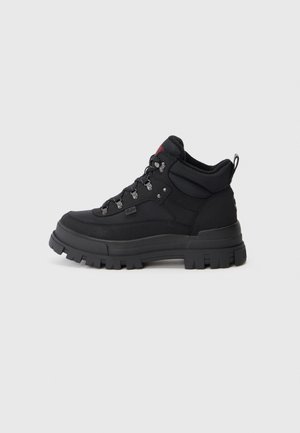 Black hiking boots made of textured fabric with a sturdy rubber sole, featuring metal eyelets, laces, and a pull tab at the back.