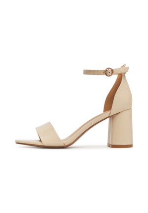 Beżowy sandał na wysokim obcasie z kwadratowym noskiem, szerokim paskiem z przodu oraz regulowanym paskiem wokół kostki, z grubym obcasem i gładką teksturą.