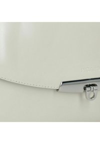 Witte leren tas met een glanzende afwerking, voorzien van een glimmende zilveren sluiting en subtiele, ingeblazen branding. Stikseldetails zichtbaar langs de randen.