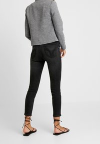 Jean skinny noir avec une finition délavée, doté de poches arrière et d'une coupe à la cheville, assorti à une veste grise texturée et des sandales noires à lanières.