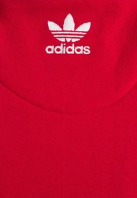 Červená bavlněná látka s kulatým výstřihem a bílým vyšitým logem Adidas se třemi pruhy nahoře.