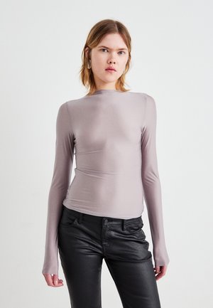 Haut à manches longues en gris clair, fabriqué dans un tissu lisse avec une coupe ajustée, présentant un col montant et des détails de couture subtils.