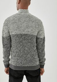 Gebreide trui in grijze gradient, met een hoge kraag en geribbelde manchetten. Gestructureerd patroon met wisselende garendikte voor extra detail.