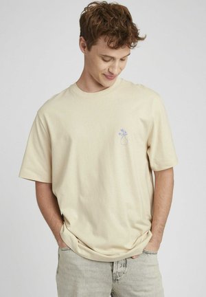 T-shirt beige à manches courtes en coton, avec un petit motif de vase violet sur la poitrine. Coupe décontractée avec un col rond.
