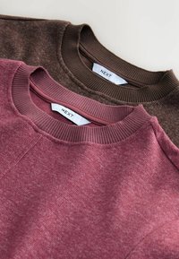 Dwie bluzy crewneck w ciemnym brązie i burgundzie. Obie mają teksturowaną tkaninę i prążkowane kołnierze, a metki są widoczne z tyłu.