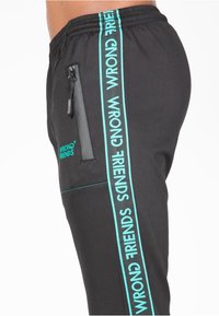 Zwarte sportieve broek met een slim fit, voorzien van turquoise zijstrepen en een ritszak. Gemaakt van glad, rekbaar materiaal.