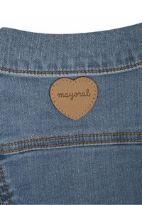 Blauwe spijkerstof met zichtbare textuur, met een bruine leren patch in de vorm van een hartje met het label "mayoral" genaaid aan de achterkant.