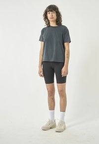 Graues Baumwoll-T-Shirt mit kurzen Ärmeln, kombiniert mit schwarzen Radshorts. Hellfarbene Turnschuhe und weiße Socken runden das Outfit ab.