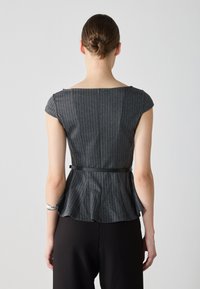 Šedý pruhovaný peplum top s krátkymi rukávmi, vykrojeným chrbtom a čiernym opaskom v páse; skombinovaný s voľnými čiernymi nohavicami. Hladká textúra látky.