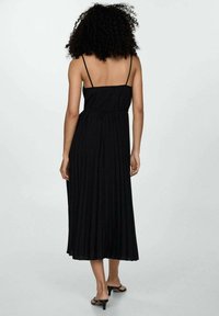 Schwarzes, plissiertes Maxikleid mit Spaghettiträgern, das eine gebundene Taille und eine glatte Textur aufweist, die unterhalb der Waden endet. Einfaches Design.